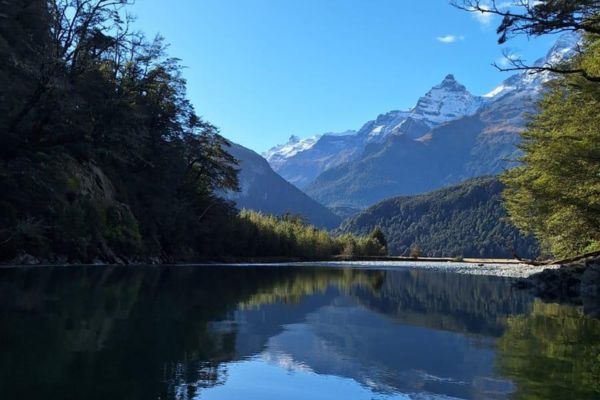 Pristine mountain river with perfect reflections of snow-capped peaks and forested valley sides