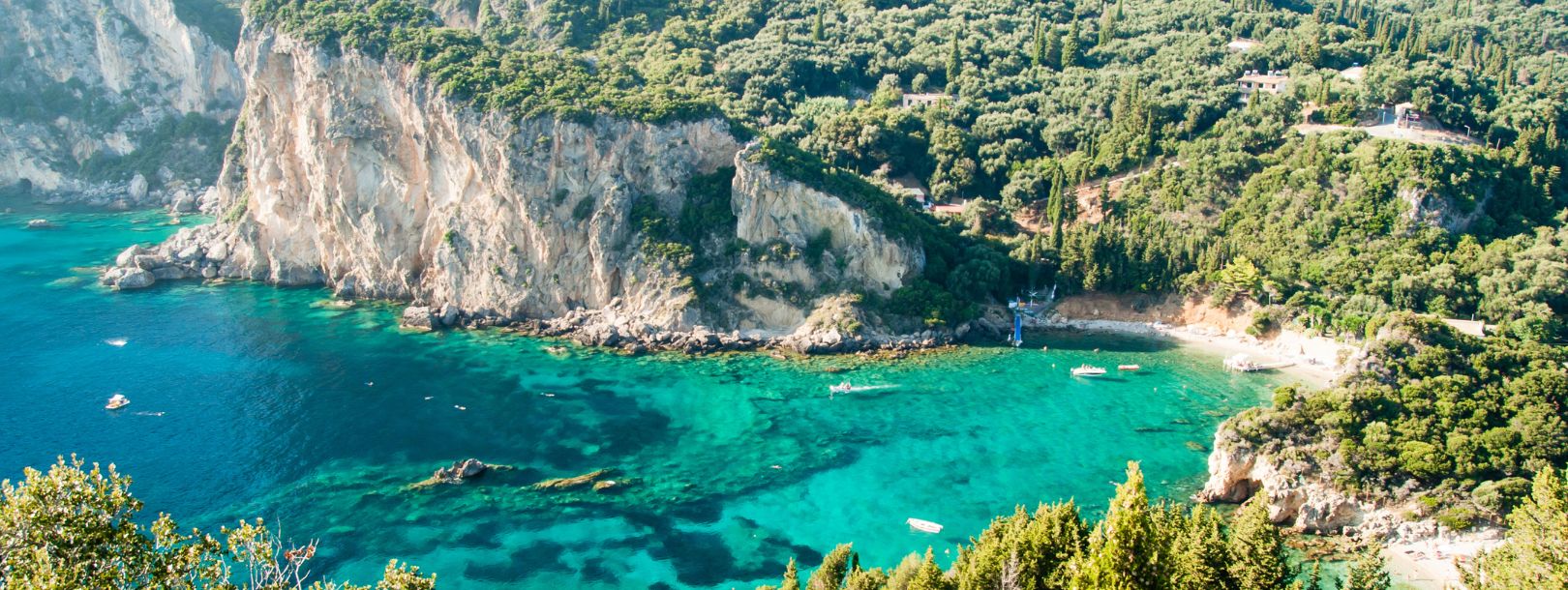 Aerial view of turquoise Mediterranean bay with white limestone cliffs, lush green hills, and small beach cove