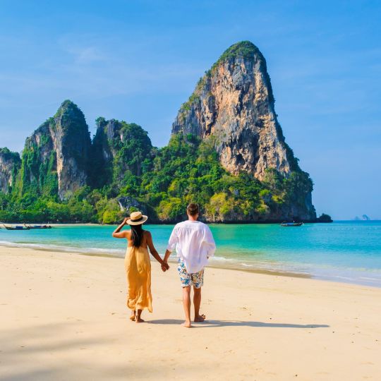 Couple on their honeymoon in a tropical location walking along the beach.