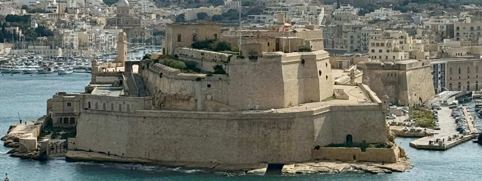 Historic fort overlooking Grand Harbour in Valletta Malta with golden-stone fortifications, turquoise Mediterranean waters and marina filled with boats showcasing UNESCO World Heritage architecture