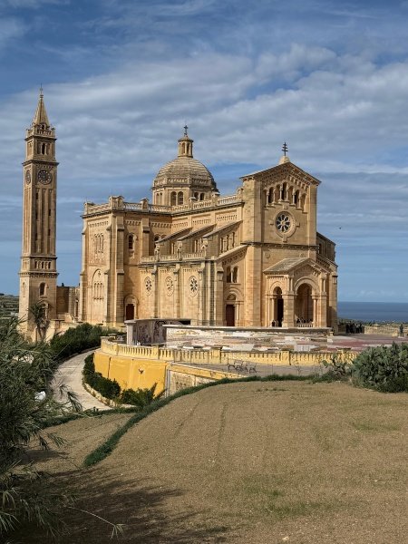 Ta' Pinu Basilica in Gozo Malta with golden-stone baroque architecture, bell tower and dome under blue Mediterranean sky showcasing iconic Maltese religious heritage