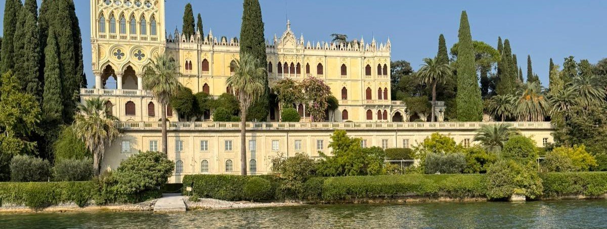 Grand lakeside villa with Gothic architecture, cypress trees and palm gardens on Lake Garda Italy showcasing elegant Italian lake escape and luxury Lake Garda holidays destination
