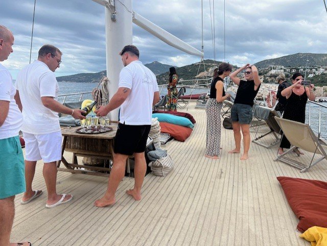 Guests enjoying complimentary gulet cruise on traditional Turkish boat in Kalkan with coastal mountains, deck dining and Mediterranean sailing experience showcasing luxury Turkey holidays
