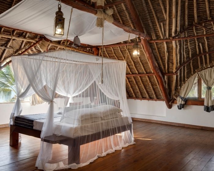Luxury four-poster bed with mosquito net canopy in a thatched safari lodge bedroom in Kenya