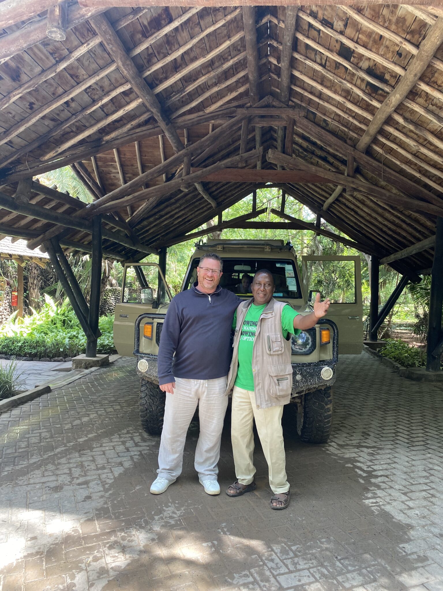 Travel guest and local safari guide posing in front of a 4x4 safari vehicle at a Kenya lodge