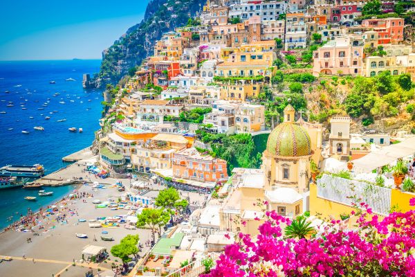 Positano village on the Amalfi Coast with colourful cliffside buildings, a domed church and pink flowers overlooking the sea