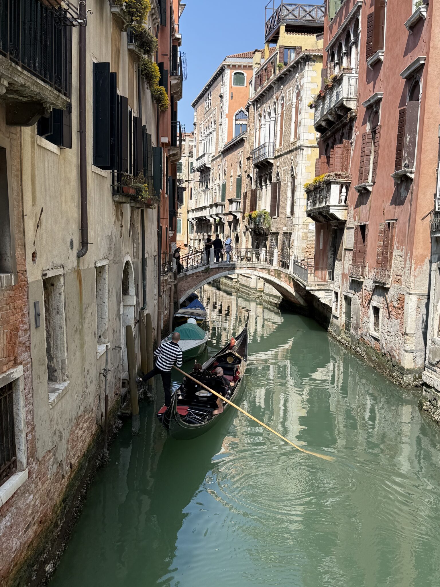 Gondolier steering a gondola along a narrow Venice canal lined with historic buildings, Italy